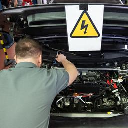 Ein Kfz-Mechaniker wartet in einer Kfz-Werkstatt ein E-Auto.